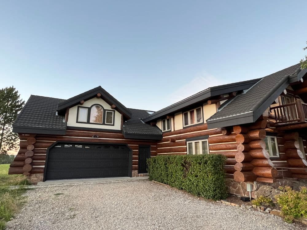 Log cabin style home with a garage, lush greenery, and clear blue sky.