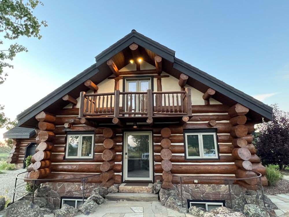 Log cabin home with balcony, stone walkway, and beautiful sky background.