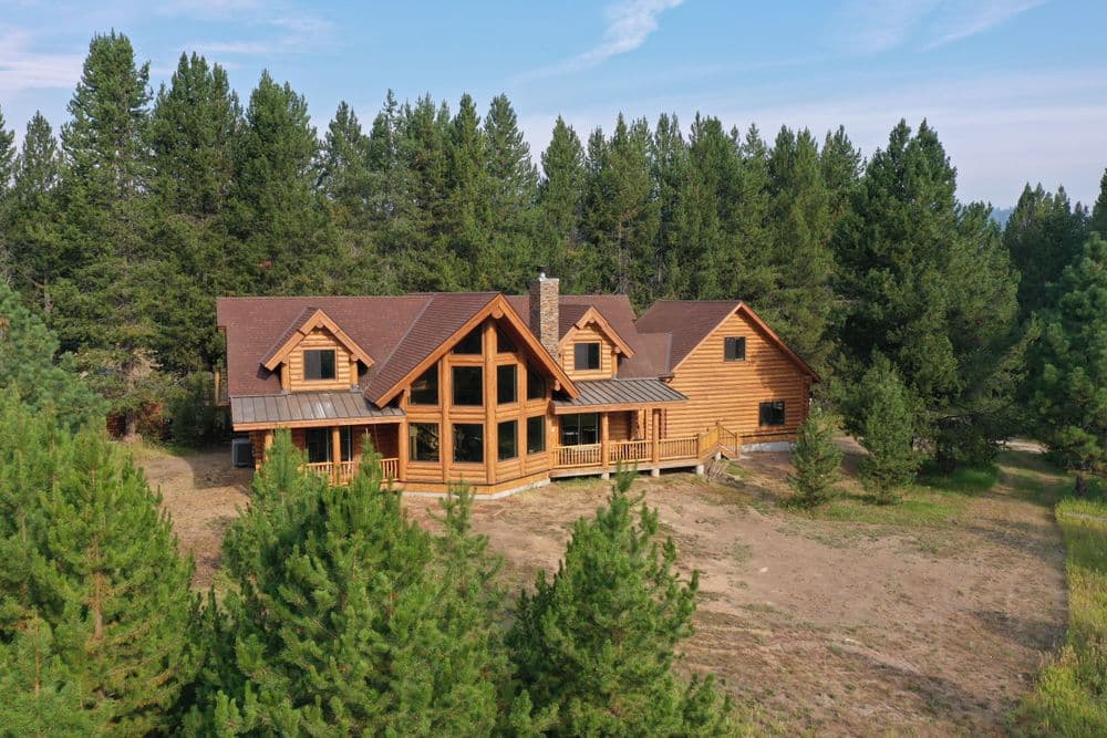 Aerial view of a spacious log cabin surrounded by lush green trees and open land.
