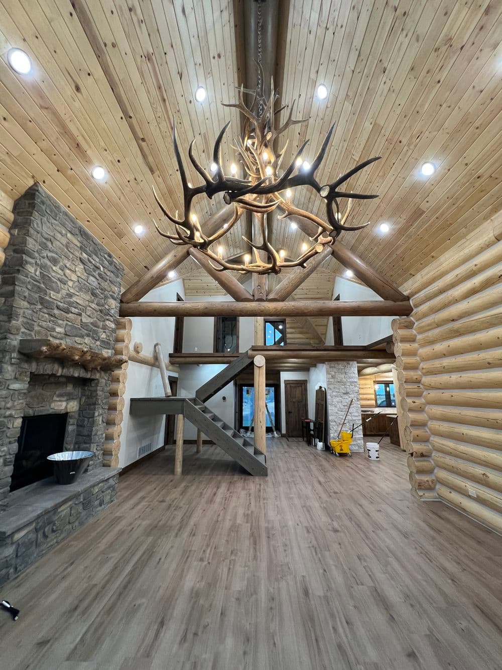 Luxurious log cabin interior with wooden beams, stone fireplace, and antler chandelier.